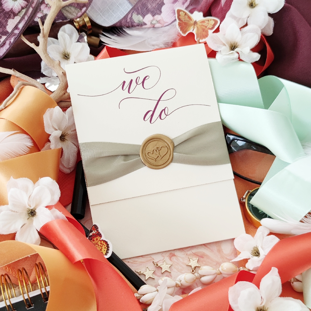 Ivory pocketfold wedding invite with light sage ribbon and gold hearts wax seal.