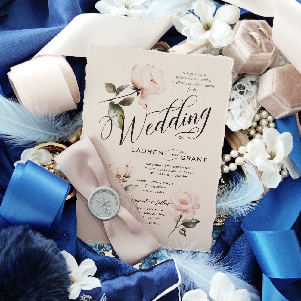Deckled edge wedding invitation with blush roses printed and a deep blush ribbon. A silver wax seal over the ribbon.