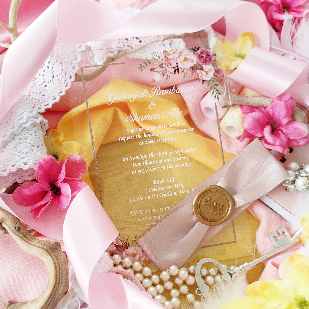 Acrylic wedding invitation with white ink and pink flowers with a deep pink ribbon and branch wax seal.