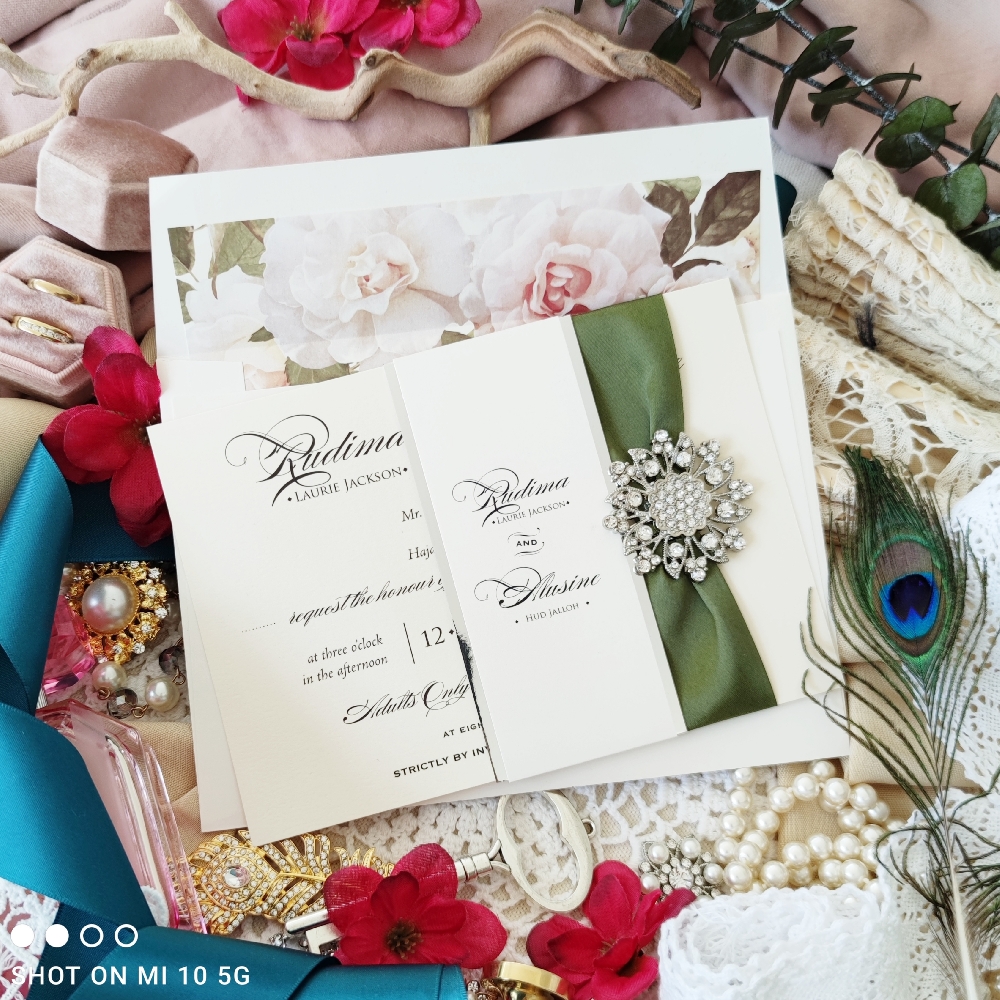 A popular invitation design using paper bellyband and sage ribbon with large rhinestone brooch.