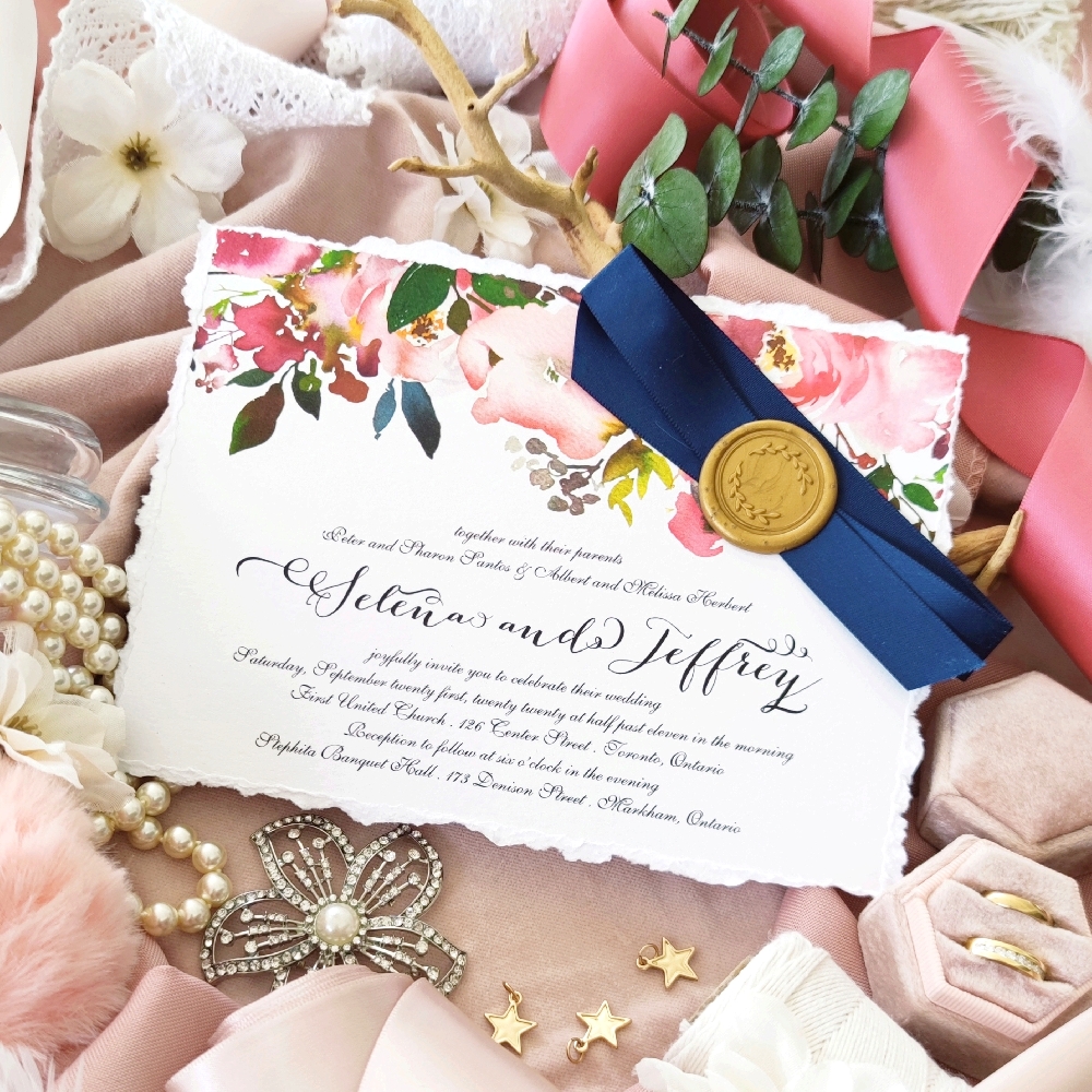 Torn edge invite with shades of pink flowers lining the top of the invite and a navy crossed ribbon with a gold wax seal.