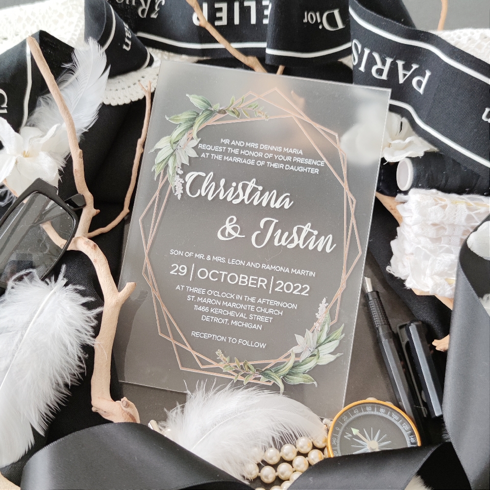Frosted acrylic invitation with white ink for the writing and a geometric shape with green foliage.