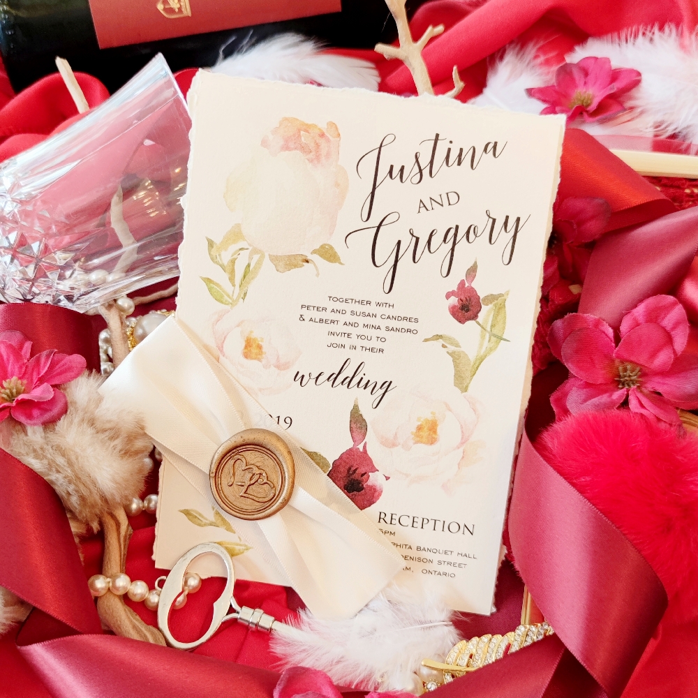 Deckled edge 5x7 wedding invite card with pink and red flowers printed and wrapped with an ivory ribbon and finished with a gold wax seal.