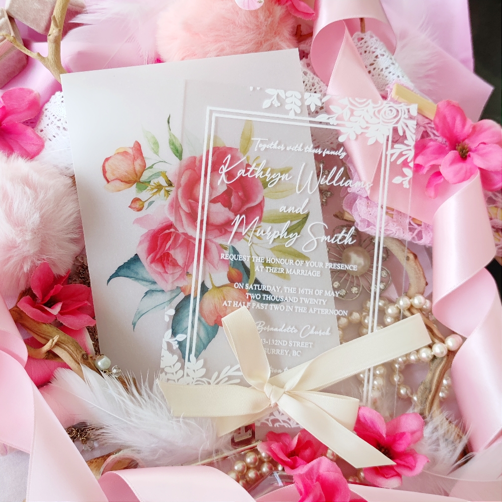 Acrylic invite with white florals at the corners and white ink with a double printed border.  A vellum wrap with bright pink flowers printed and tied together with a blush bow.