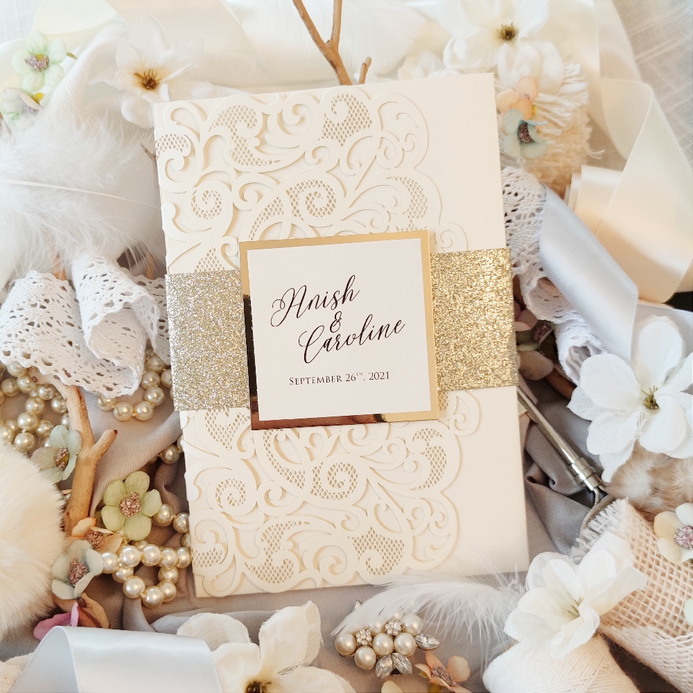 Three fold lasercut wedding invite with full champagne glitter bellyband and a square tag with bride & groom\'s names printed.