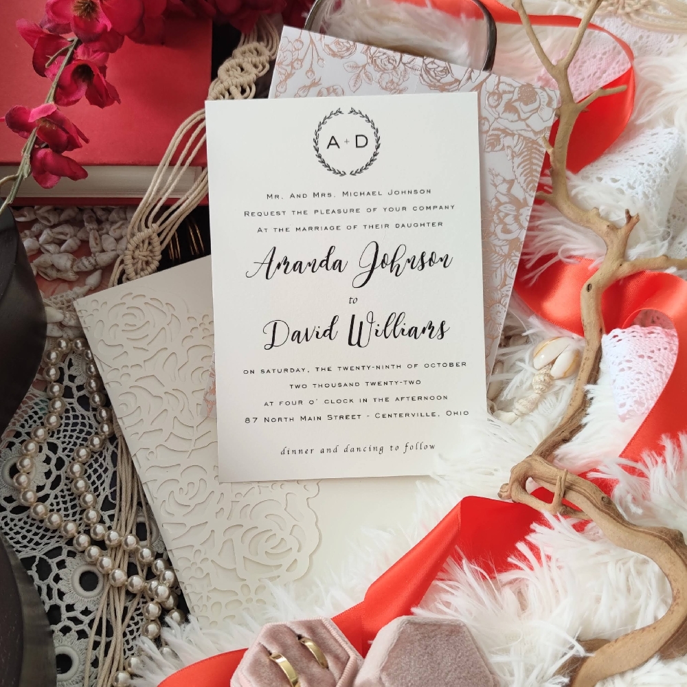 An ivory rose patterned lasercut wedding invitation opens into a three fold card with the main wording in the centre and a pocket on the right side.