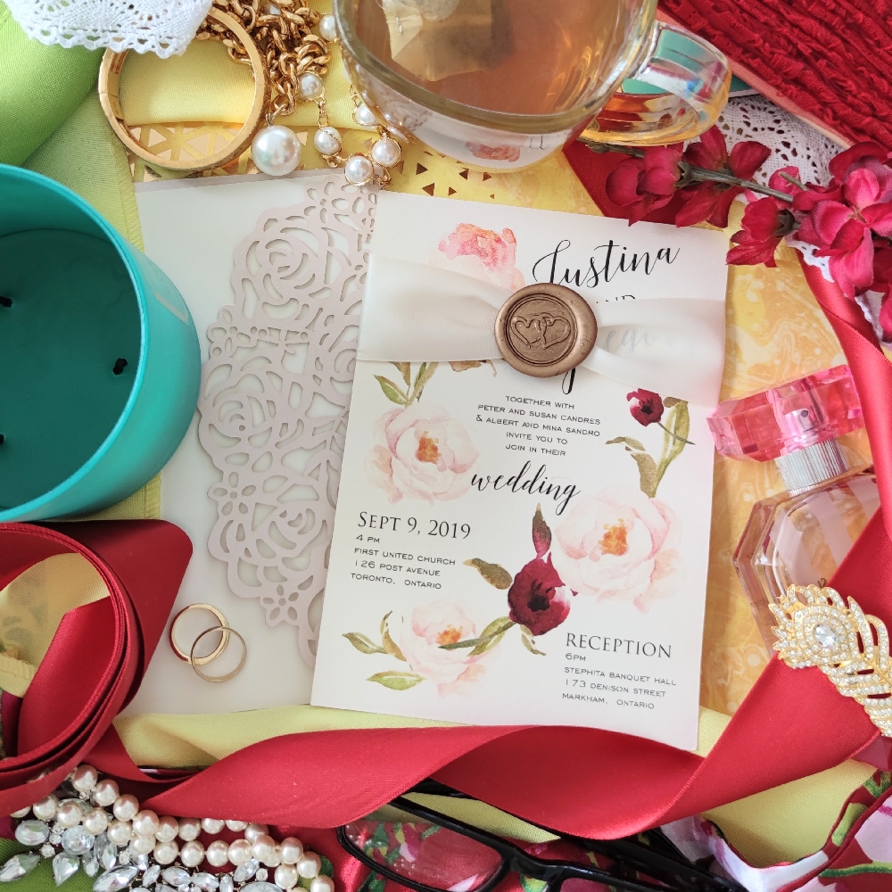 Blush pink roses printed on an ivory invitation card with a pink ribbon and gold wax seal.