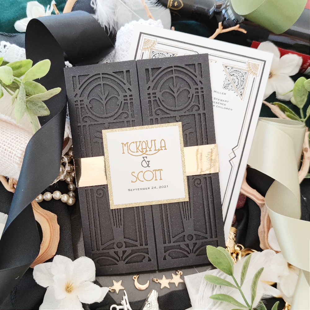 This black lasercut wedding invitation has a gold mirror band around the card and a tag with the bride and groom\'s names printed.  There is also a champagne gold glitter matting behind the couple\'s name.