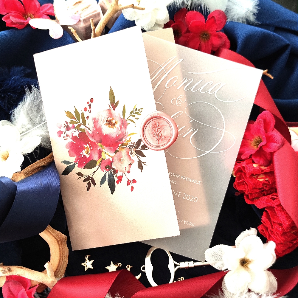 This photo shows two invitation styles.  There is a pocket fold blush invitation card with a blush wax seal as well as a vellum UV printed flat single card.