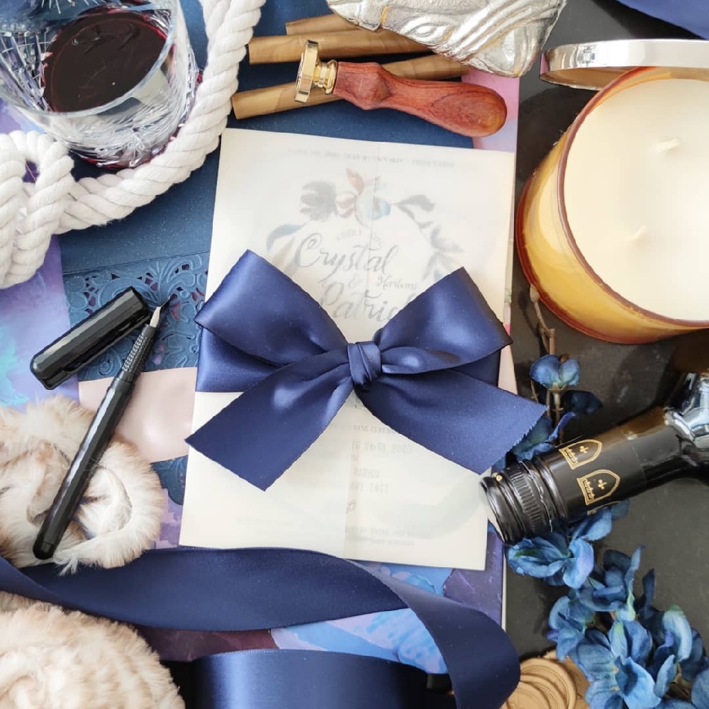 A vellum wrapped gate fold wedding invitation with a thick navy bow.