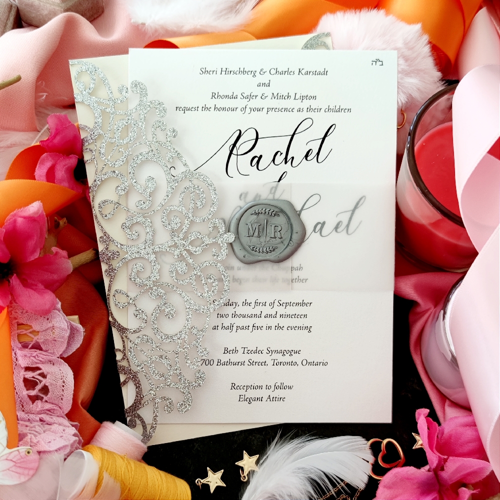 This invitation card has a vellum bellyband around it with a silver wax seal.  The wedding card behind is a silver glitter lasercut design.