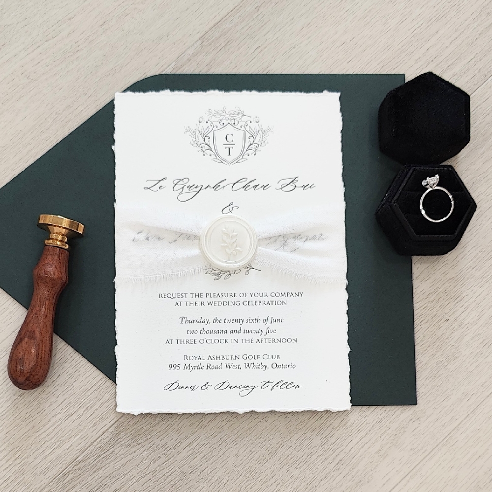 This is a deckle edge wedding invite wrapped with a ruched ribbon and wax seal embellishment.  It is paired with a black envelope.