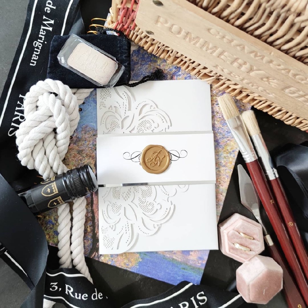 A white laswercut wedding invitation with a gold monogram wax seal on a bellyband wrap.