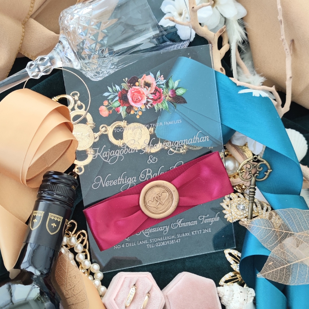 A clear acrylic design with a wine ribbon ruched around the invite and a gold hearts wax seal.