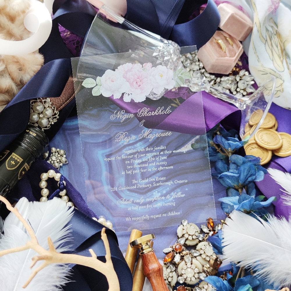 Rectangle acrylic wedding invite with pink flowers top center and gold writing.