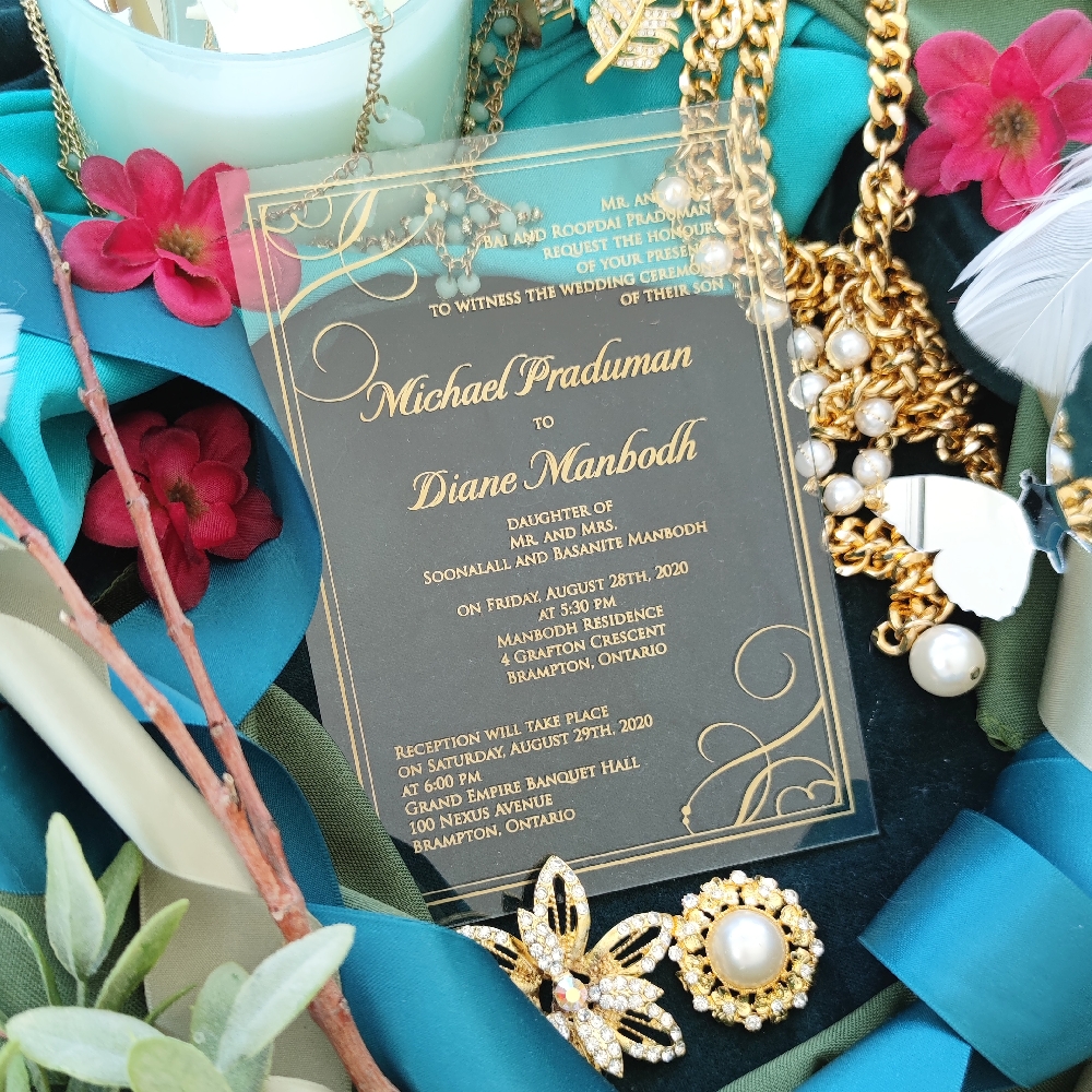 A clear acrylic wedding invitation with gold foil printed writing.