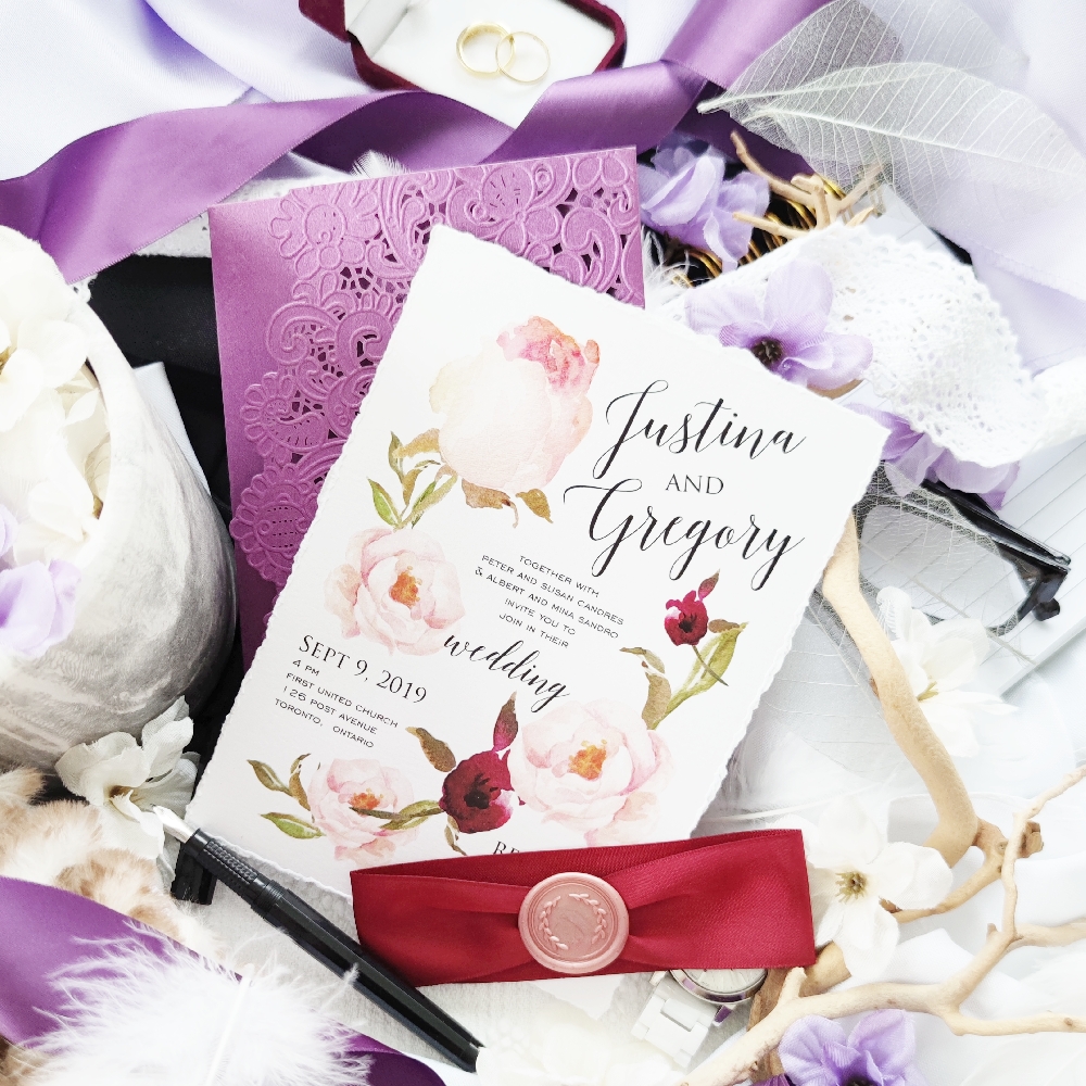 Torn edge invitation card with deep red ribbon and blush wax seal.