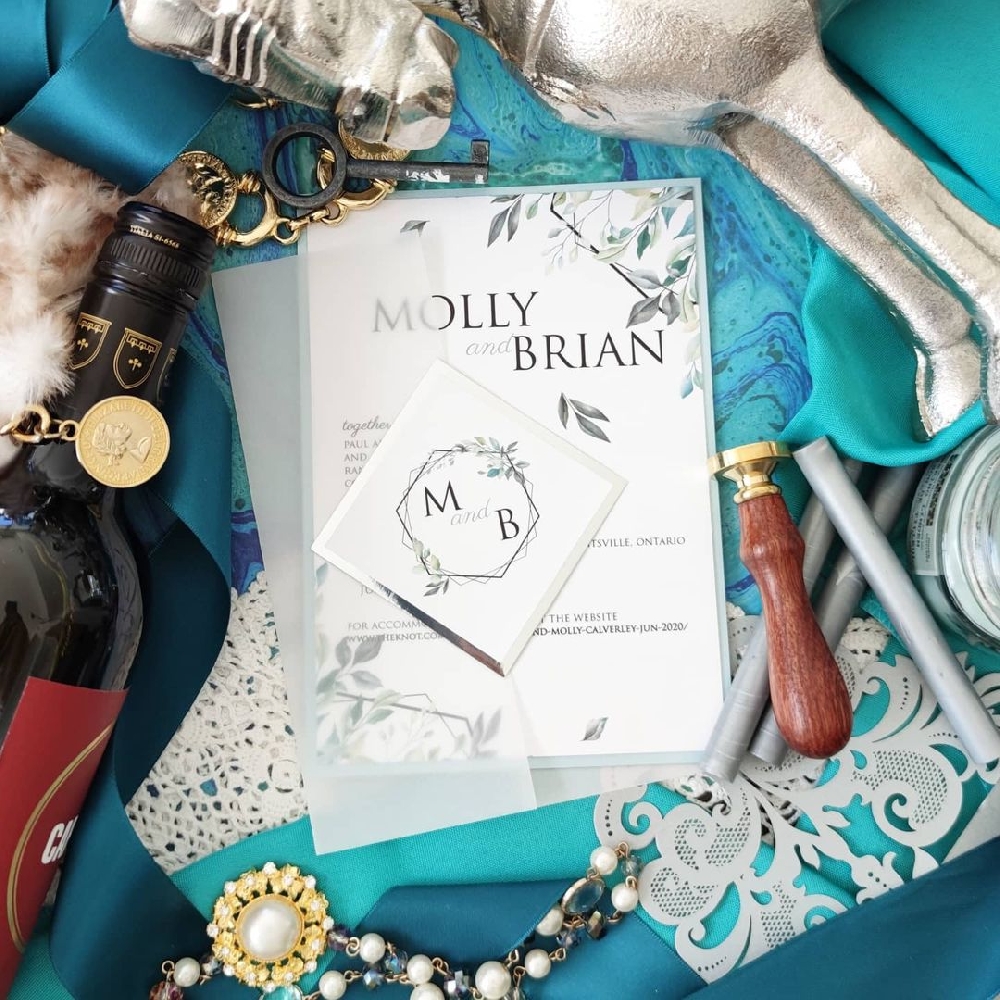 A vellum wrapped wedding invite with blue and green accents.