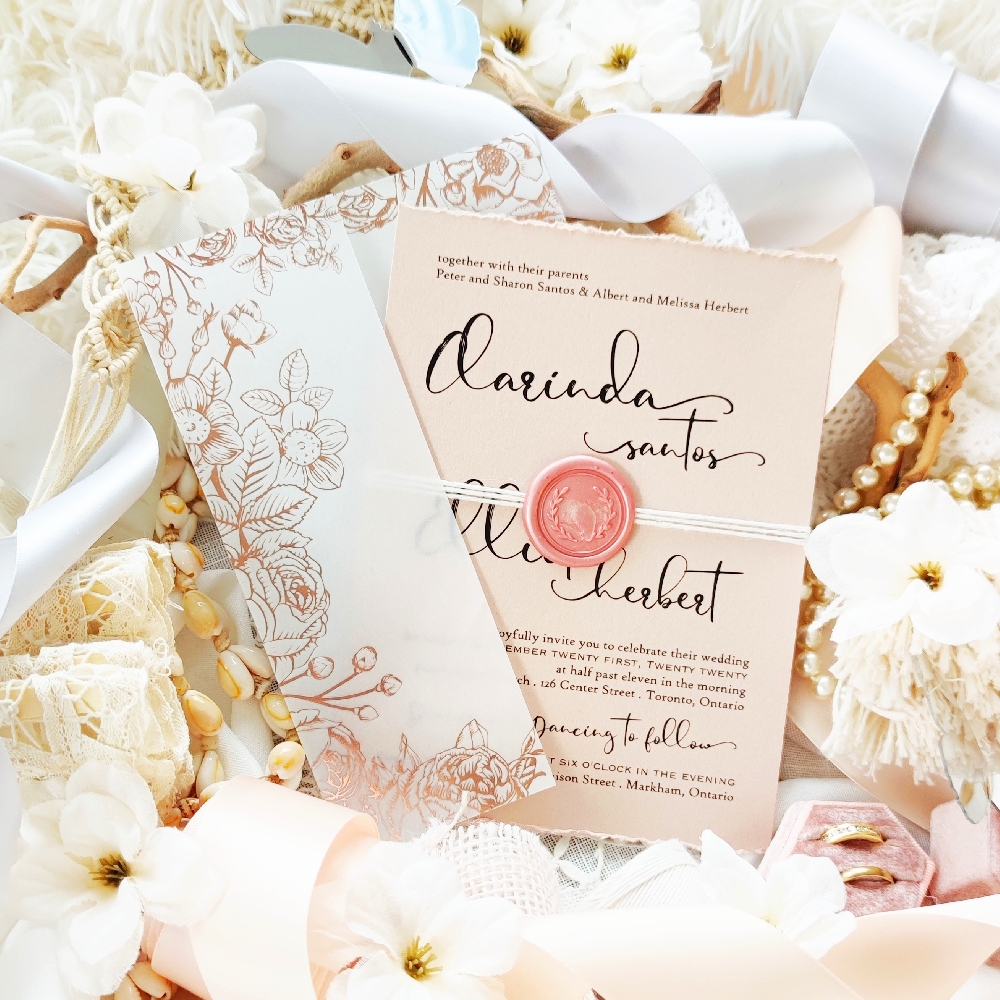 Blush pearl wedding invitation with black fonts and a white string with a blush wax seal.