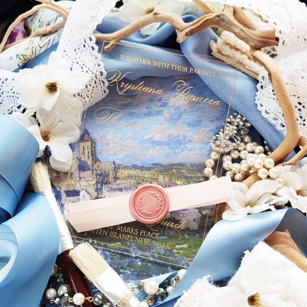 Clear acrylic wedding invitation with gold screen printing and a thin ribbon wrap with wax seal.