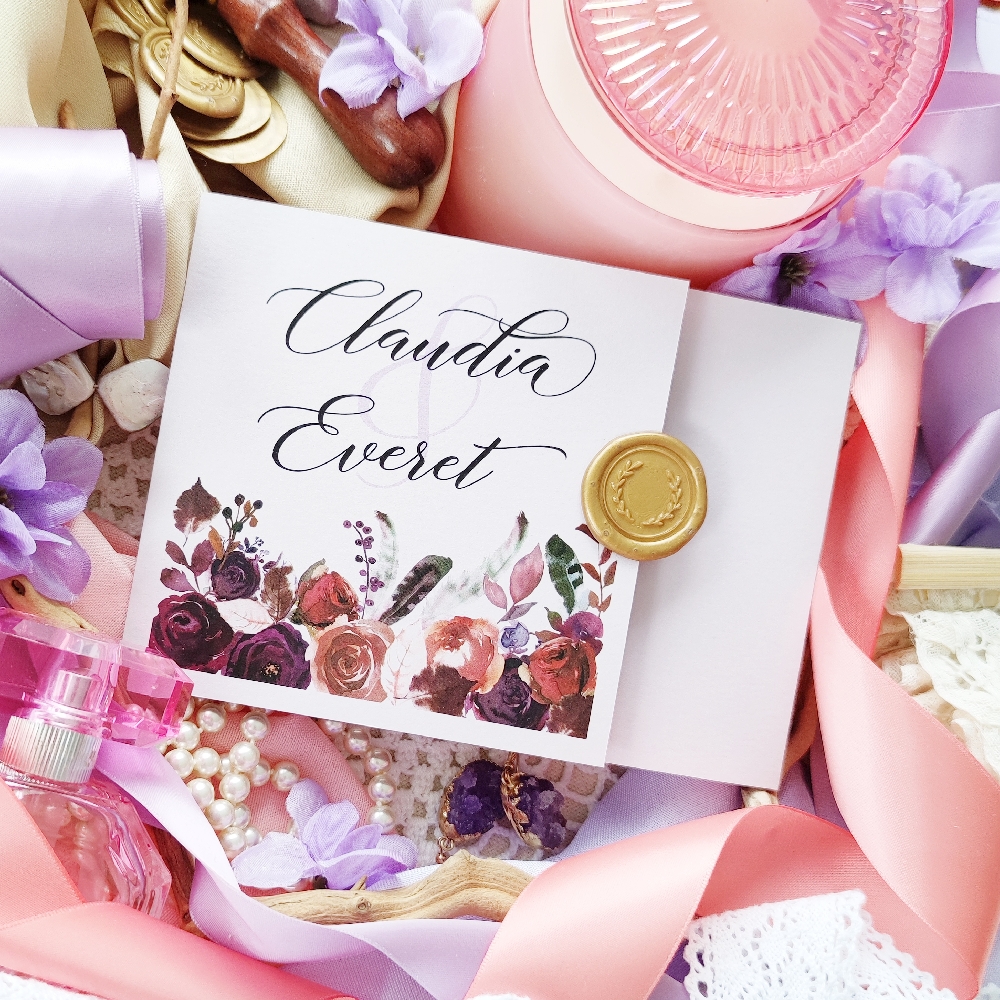 A three fold wedding invitation card with flowers printed along the bottom and a wax seal added.